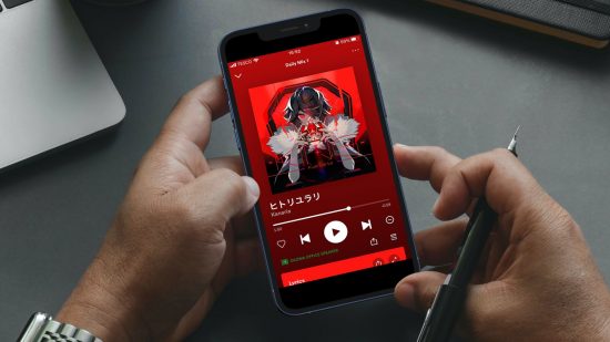 Spotifyとは：スマートフォンを両手で持っている写真。 電話には、King by Kanaria を再生している Spotify 音楽プレーヤー画面が表示されています。