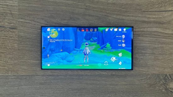 Samsung Galaxy S23 Ultra のレビュー ヘッダーには、原神がプレイされている携帯電話の画面が表示されており、携帯電話は木製の表面に平らに置かれています。