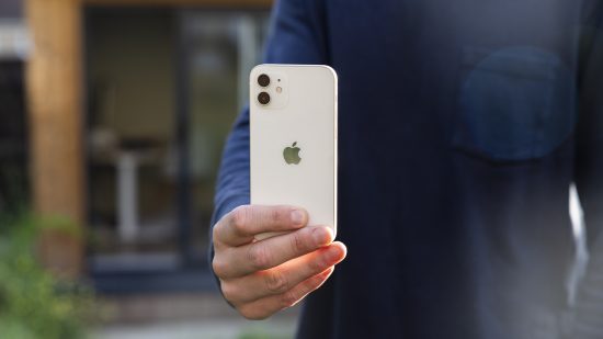 屋外で男性の手に握られている白いiPhone 12