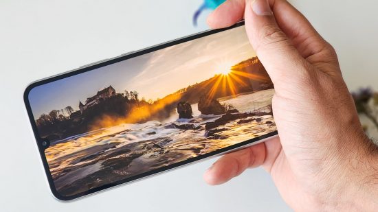 携帯電話のレビュー用に、湖に沈む夕日を映した Samsung Galaxy A34 のディスプレイの写真